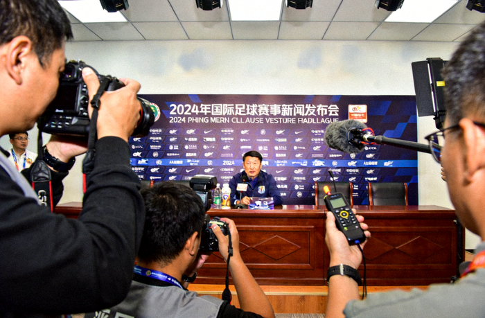 体育新闻发布现场，记者手持设备记录赛事相关信息